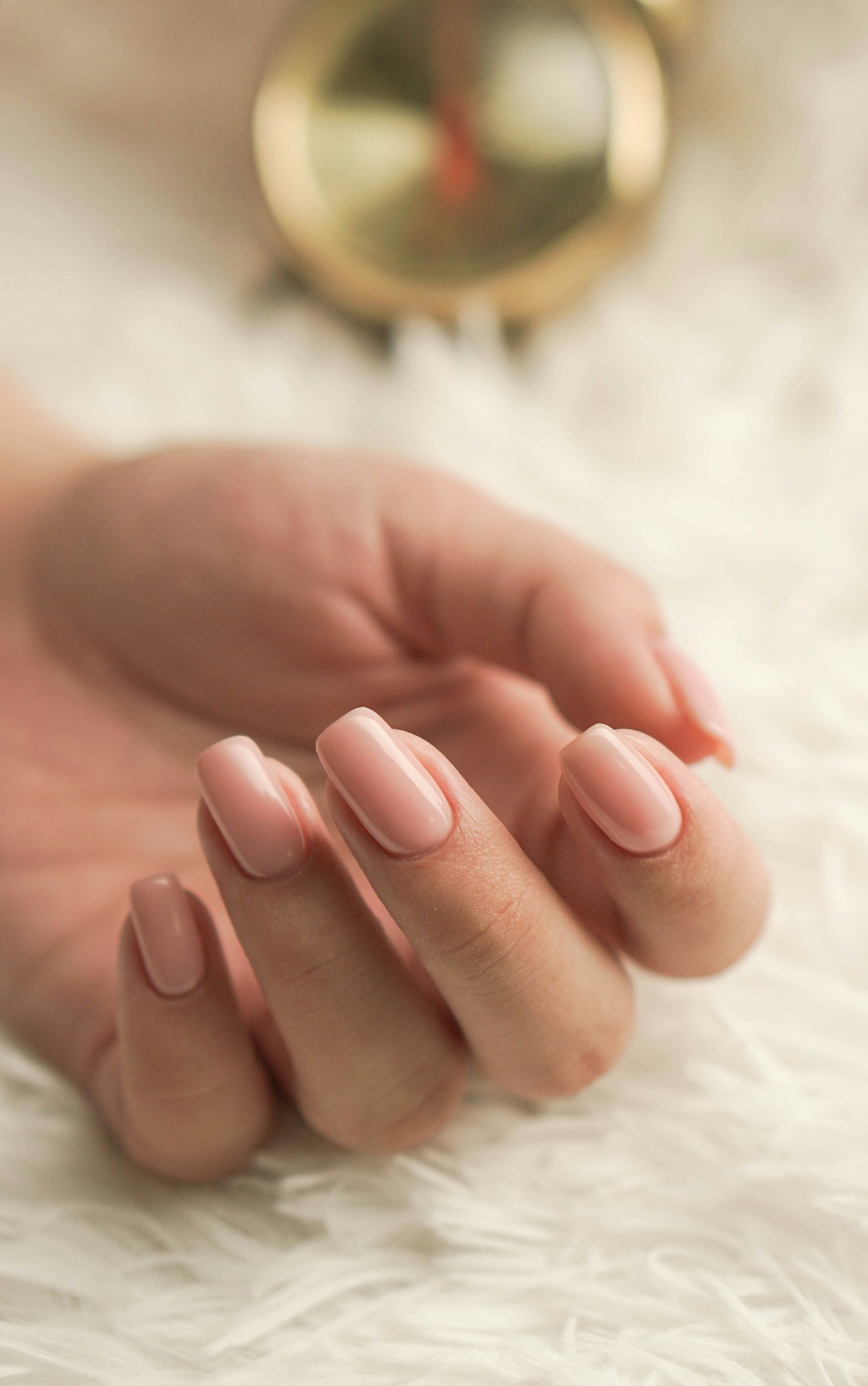 A hand with light pink manicured nails resting on a soft white surface